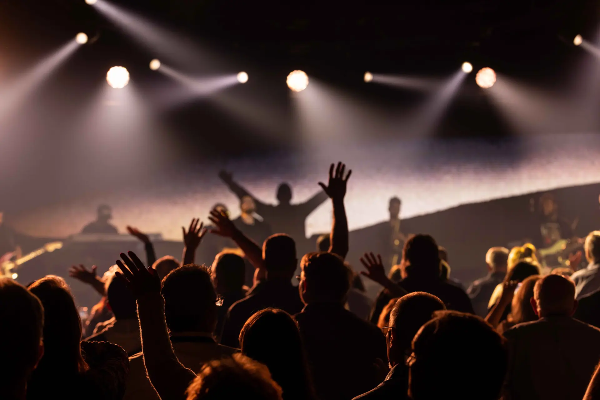 A crowd of people in front of lights and one person is raising his hands.