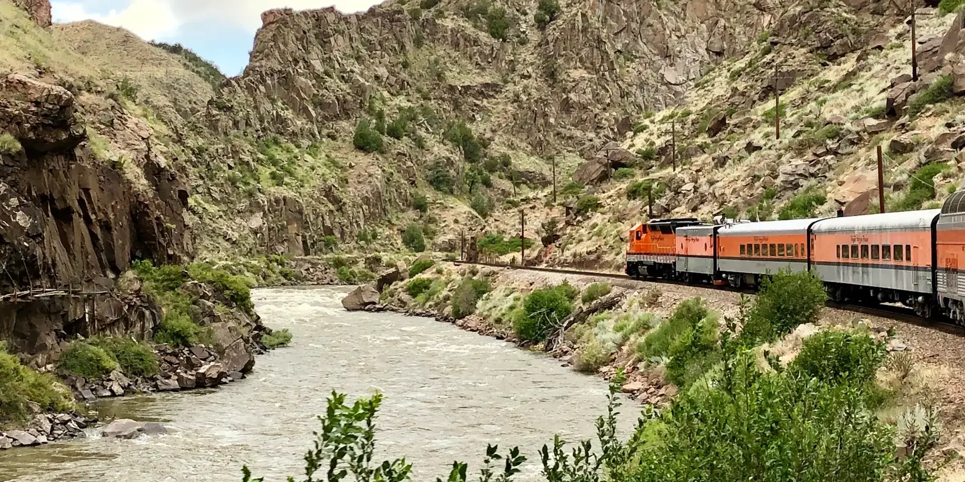 A train traveling through the mountains near water.